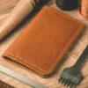 A leather wallet beside waxed thread and cutting tools