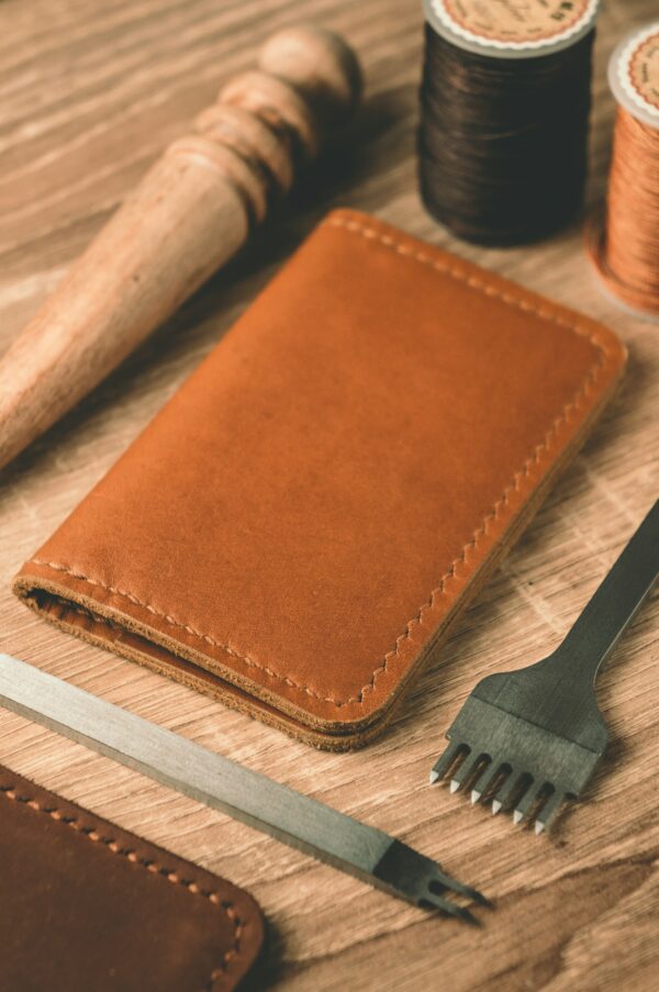 A leather wallet beside waxed thread and cutting tools