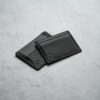 The Bifold Black leather bifold wallet on a pale surface